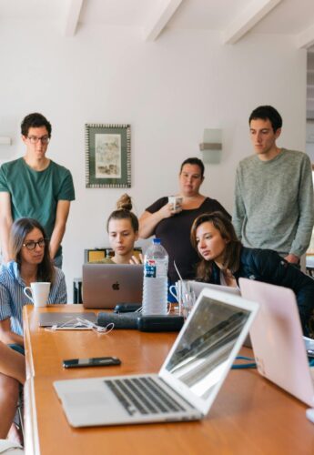 A group of young people gather around their laptops discussing