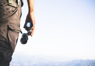 Tourist is holding through binoculars on sunny cloudy sky from m
