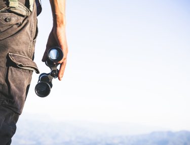 Tourist is holding through binoculars on sunny cloudy sky from m