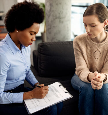 Black female counselor taking notes while having conversation with another woman