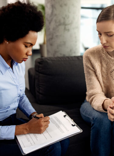 Black female counselor taking notes while having conversation with another woman