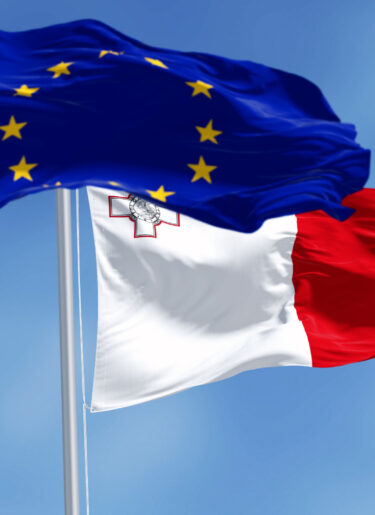 Flags of Malta and the European Union waving in the wind on a clear day.
