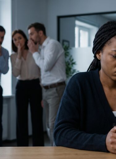Sad African American black businesswoman feeling isolated while colleagues gossip during coffee break, concept for workplace discrimination