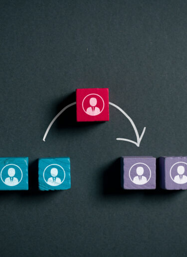 Wooden employee icon moving between two teams, representing workforce mobility, reassignment, talent transfer, organizational change and internal career transition.