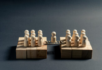 Wooden miniature figure standing on a bridge between two business teams, symbolizing mediation, negotiation, communication and organizational alignment.