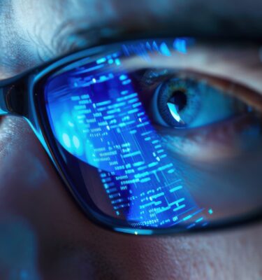 Smart glasses reflecting digital data stream over eye of man working in dark blue lighting.