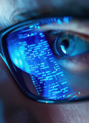 Smart glasses reflecting digital data stream over eye of man working in dark blue lighting.