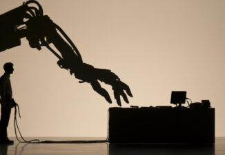 Silhouette of a man facing a giant robotic arm at a desk