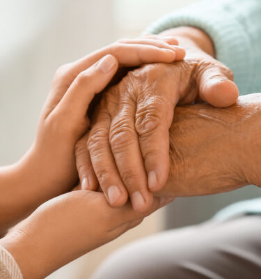 Senior woman with daughter holding hands at home, closeup