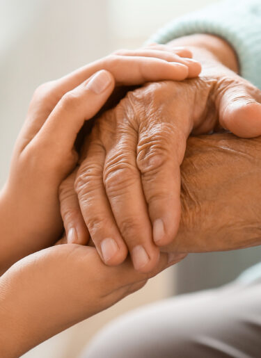 Senior woman with daughter holding hands at home, closeup